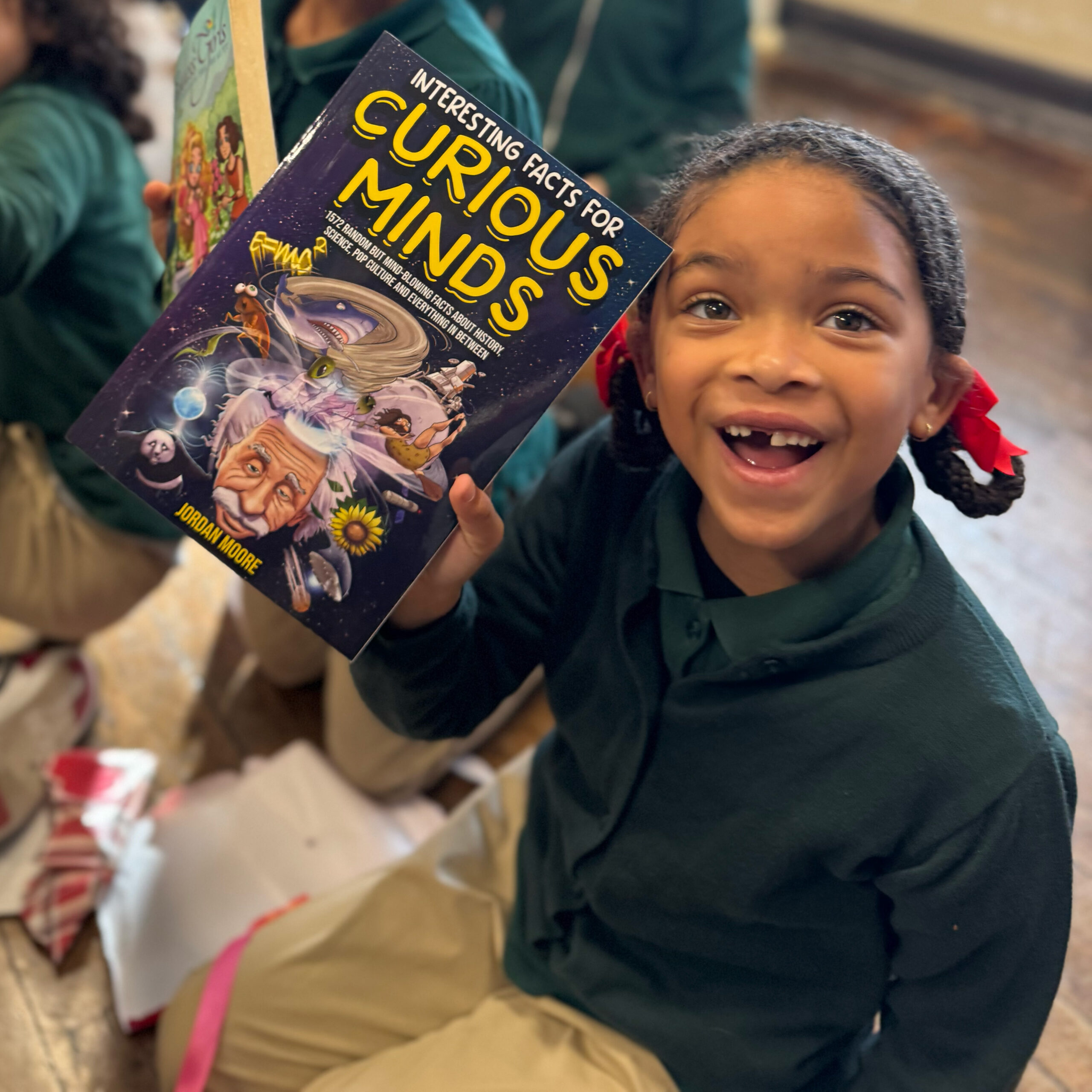 Nebinger Student Excited About Reading Smiling student at George W. Nebinger School in Philadelphia holding a “Curious Minds” book during a classroom reading activity.